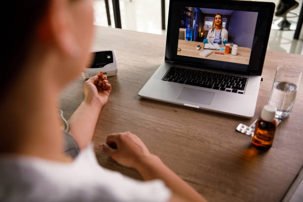 Woman talking with her doctor over video conference and measuring blood pressure Over the shoulder view of woman measuring her blood pressure while video chatting with her doctor. Online Therapy for Addiction of 2023 stock pictures, royalty-free photos & images