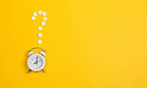 Photo of Contraception Day contraceptive pills with alarm clock on yellow background.