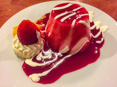 Vanilla panna cotta covered in raspberry coulis with strawberry, mango and cream