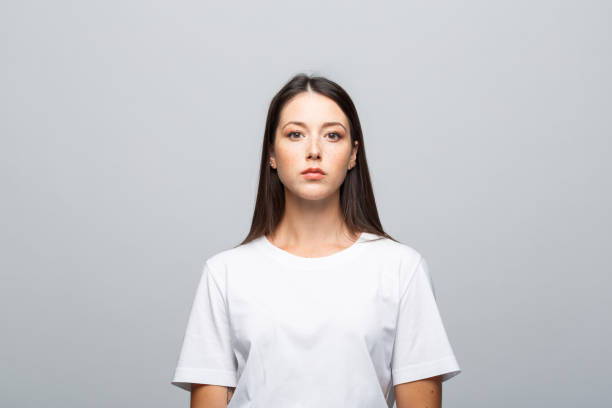Headshot of confident young woman Portrait of beautiful young woman wearing white t-shirt, looking at camera. Studio shot, grey background. blank expression stock pictures, royalty-free photos & images