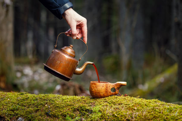 A man pours delicious coffee from vintage kettle into wooden cup on mossy old tree. A man pours delicious coffee from vintage kettle into wooden cup on mossy old tree. Forest background blurred. coffee crop photos stock pictures, royalty-free photos & images
