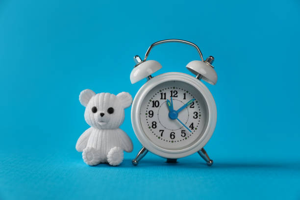 istock Alarm clock and toy bear on light blue background. Time to give birth 1320314595
