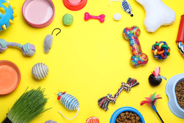 Different pet toys and feeding bowls on yellow background, flat lay. Space for text