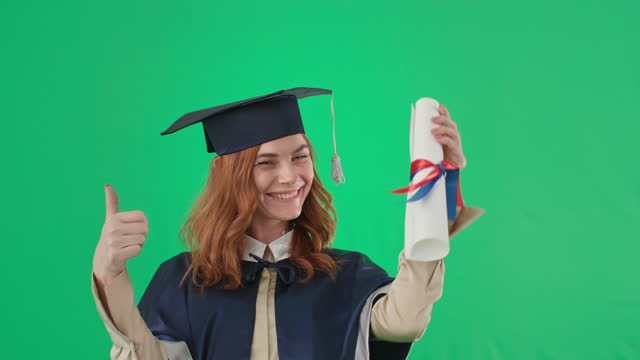 graduation online, portrait of an emotional joyful girl in academic clothes with diploma smiling and showing hand to class and camera on green screen background, chroma key