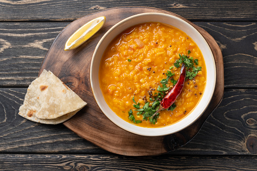 Masoor dal. Indian spicy red lentil soup, roti (chapati) are on brown wooden table.