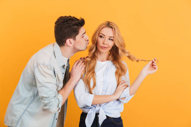 retrato de una mujer encantadora mirando a un lado y vacilando mientras el hombre trataba de besar su mejilla, aislado sobre fondo amarillo - hesitating fotografías e imágenes de stock