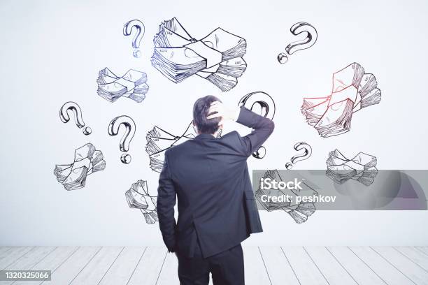 Earning Money And Business Idea Concept With Pensive Businessman Looking At White Wall With Handwritten Sketch Of Money Packs And Question Marks Stock Photo - Download Image Now