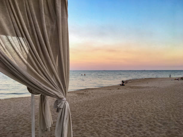 A man in the distance sits on a sandy beach A man in the distance sits on a sandy beach and looks at the calm sea and the sunset. Evening Sandy beach in Mariupol on the Sea of Azov mariupol stock pictures, royalty-free photos & images