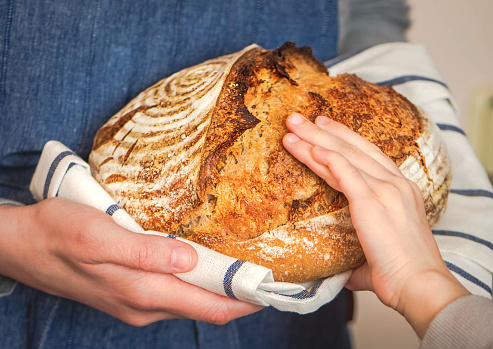Hands of mother and daughter touching a loaf of freshly baked rustic bread. Concept of family and healthy food.