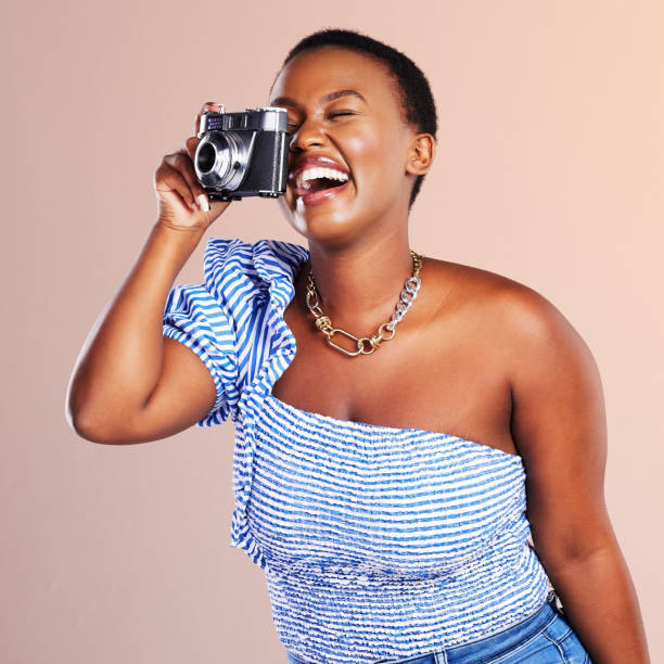 Studio shot of a beautiful young woman using a camera against a oink background