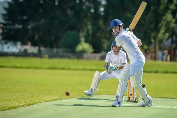 Male batsman hitting the ball while wicket-keeper standing behind stumps on the pitch.
