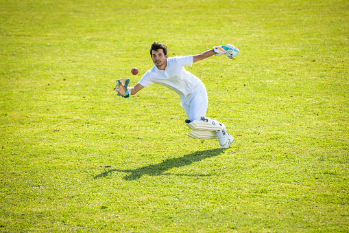 Young male wicketkeeper diving to the side and catching the cricket ball on the field.