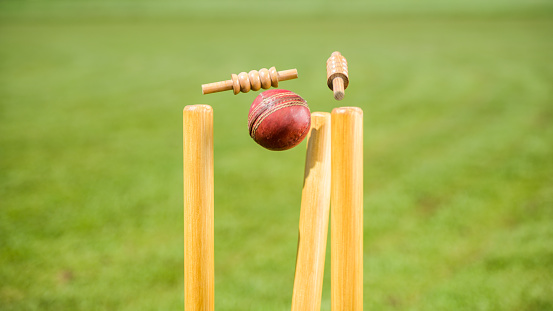 Close-up of cricket ball hitting the stumps and knocking off the bails on the field.