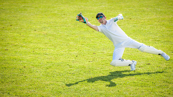 Wicketkeeper diving to the side and catching the cricket ball on the field.