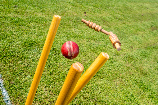 Close-up of cricket ball hitting the stumps and knocking off the bails.