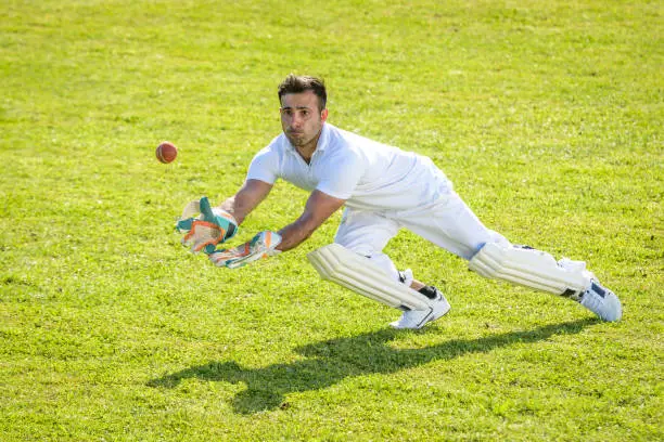 Young male wicketkeeper catching the ball on the field.