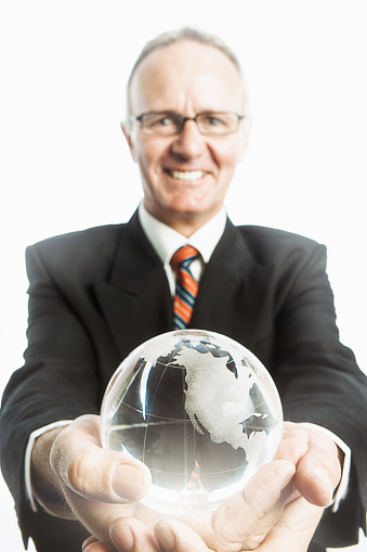 Well-dressed businessman holds a crystal glass world globe, representing global business.