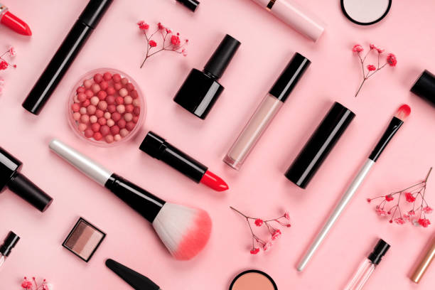 various cosmetic accessories for makeup and manicure on trendy pastel pink background with red flowers. blush, brush, eye shadow, mascara, perfume, lipstick, nail polish. skin care products. - make up imagens e fotografias de stock