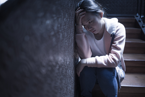 young beautiful Asian woman in pain suffering depression - dramatic indoors portrait on staircase of sad and depressed Japanese girl as victim of bullying and abuse