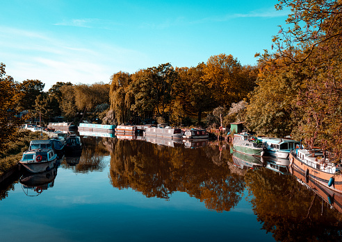 Peaceful image depicting houseboats and barges moored up on a calm, still river in the Lea Valley in London, UK.