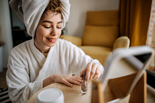 Young woman in a bathrobe is sitting and varnishing her nails