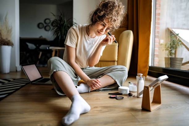 I want to be even more beautiful Young beautiful woman is sitting in her living room and putting on make-up applying stock pictures, royalty-free photos & images