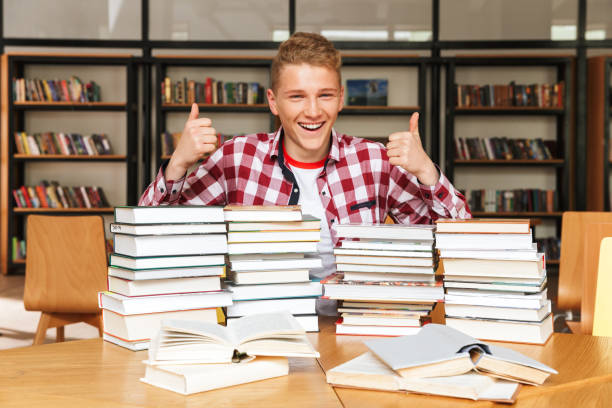 istock Smiling teenage boy sitting at the library table 1320352023