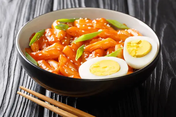 Korean street food Tteokbokki or dukbokki cooked in spicy sauce served with boiled eggs and green onion close-up in a bowl on the table. horizontal