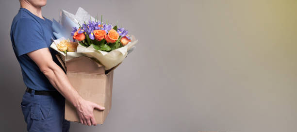 istock White male courier holding a large box with several bouquets. Delivery concept. 1320353812