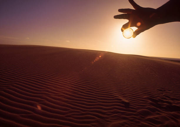 istock Man's hand holding camera filter in front of sun in the desert at sunset 1320356384