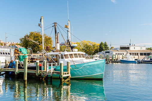 Photo of a fishing boat moored to a wooden pier in a harbour on a clear autumn day. Reflection in water. Hyannis, Cape Cod, MA, USA.