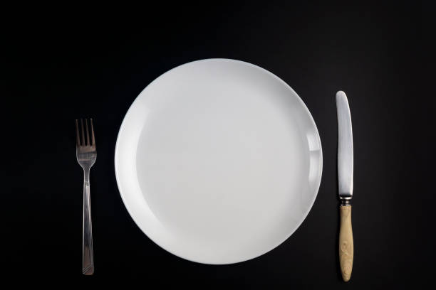 istock Fork, knife and white plate on black background in flat lay 1320360594