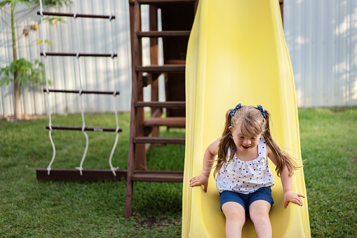 Little blond girl going down on a slide in her backyard