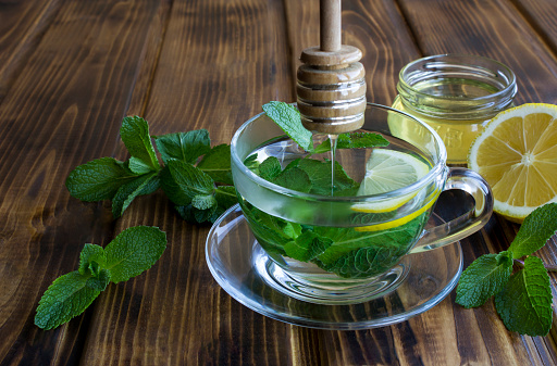 Mint tea with honey  in the glass cup on the wooden background. Close-up.