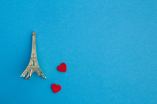 Two small red hearts and eiffel tower souvenir on the blue background. Top view. Copy space.