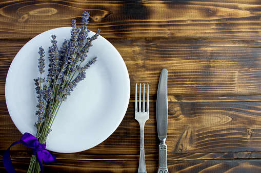 Table setting with the white plate and dried lavender on the brown wooden background. Top view. Copy space.