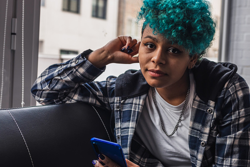 young woman or girl with mobile phone at home or apartment with blue hair afro american curl
