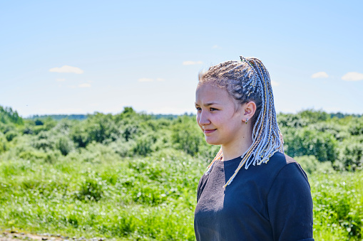 Portrait of a cute Asian smiling girl of the generation of zoomers with dreadlocks on her hair on the background of nature.