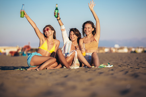 Happy young women sitting on the beach. Group of friends enjoying on beach holiday.