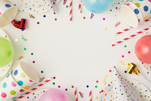 Top view photo of party table decoration paper plates cups hats straws pipes balloons sequins and confetti on isolated white background with copyspace in the middle