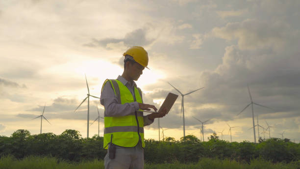 istock Portrait of Asian windmill engineer man, worker working, using a computer laptop on site at wind turbines field or farm, clean energy source. Eco technology for electric. industry environment. People 1320376245