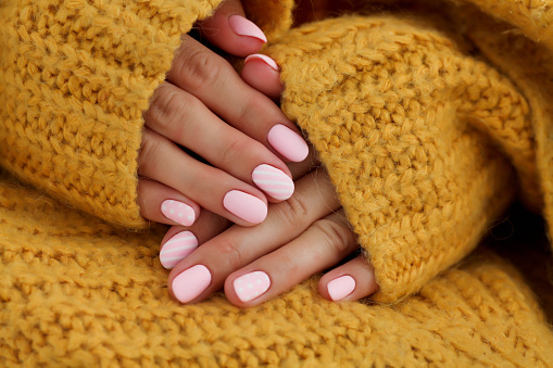 Manos femeninas con hermosas uñas de forma ovalada, manicura rosa mate primer plano sobre un fondo de suéter de punto. goma laca. Espacio de copia photo
