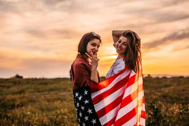 istock Two women  covering themselves with USA flag on meadow 1320377607