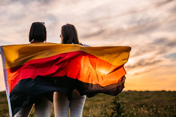 zwei frauen bedecken sich mit deutschlandfahne auf wiese - tag der deutschen einheit stock-fotos und bilder
