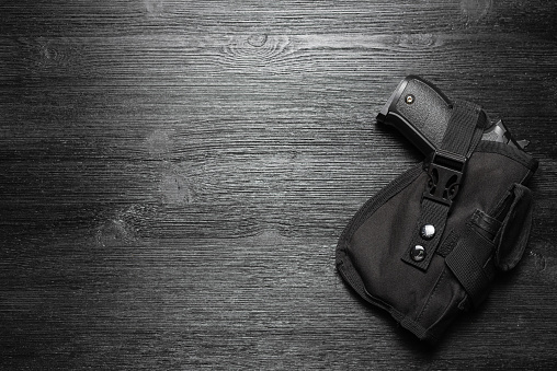 Airsoft gun in the holster on the black flat lay background with copy space.
