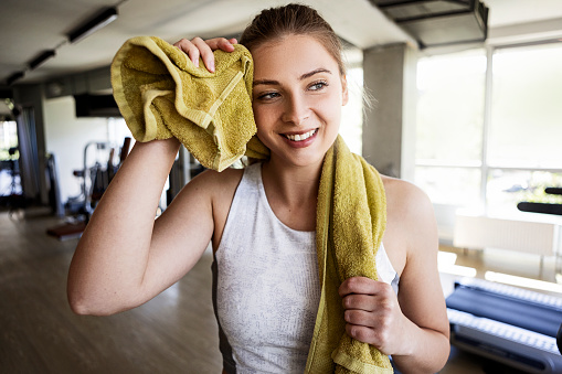 Smiling young fitness girl holding a towel in gym around neck