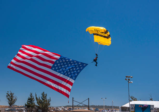 Army parachute landing in arena at Rodeo Santa Maria, CA, USA. Santa Maria, CA, USA - June 6, 2010: Rodeo. Closeup of Yellow Army parachute landing in arena with large US flag on foot in blue sky. santa maria california photos stock pictures, royalty-free photos & images