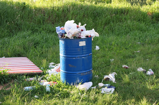 An iron tank filled with waste, garbage scattered around on the grass.