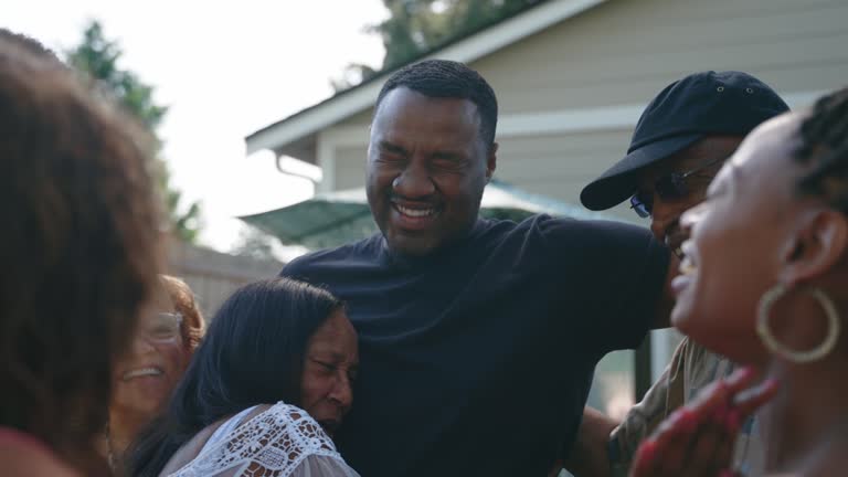 A large multi-generational group of family relatives greets and embraces in the backyard having not seen each other for a long time, due to normal circumstances or perhaps COVID-19 or Coronavirus. Happiness and joy abound as they are together again.
