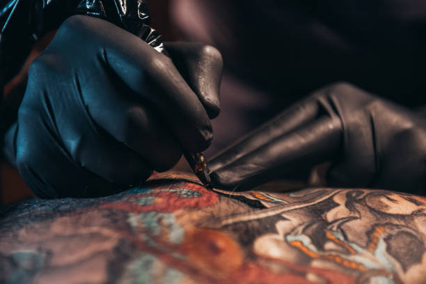 mani di un tatuatore che indossa guanti neri e tiene in mano una macchina - tatuare foto e immagini stock